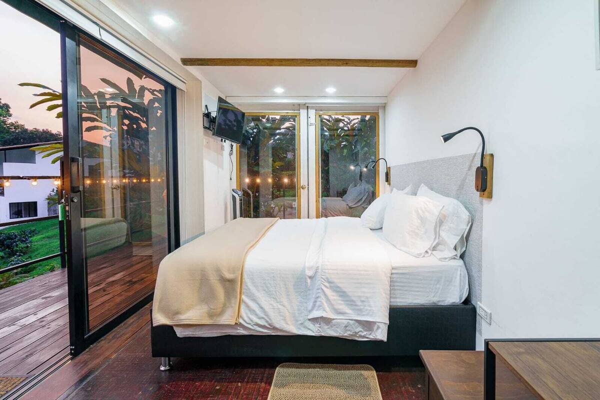 Un dormitorio moderno con una cama grande, un ventanal corredero que da a un espacio exterior y un televisor instalado en el techo.