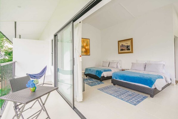 A balcony with a table and chairs, two beds with blue bedding, and a painting on the wall. - ACAIMA CAFE (Sasaima)