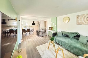 Ein modernes Wohnzimmer mit einem grünen Sofa, einem Couchtisch und einem Essbereich mit Stühlen und einem Tisch.