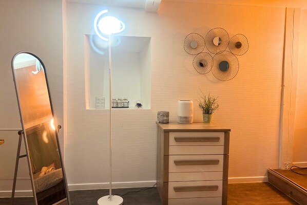 A room with a standing mirror, a floor lamp, a dresser, and wall decor.