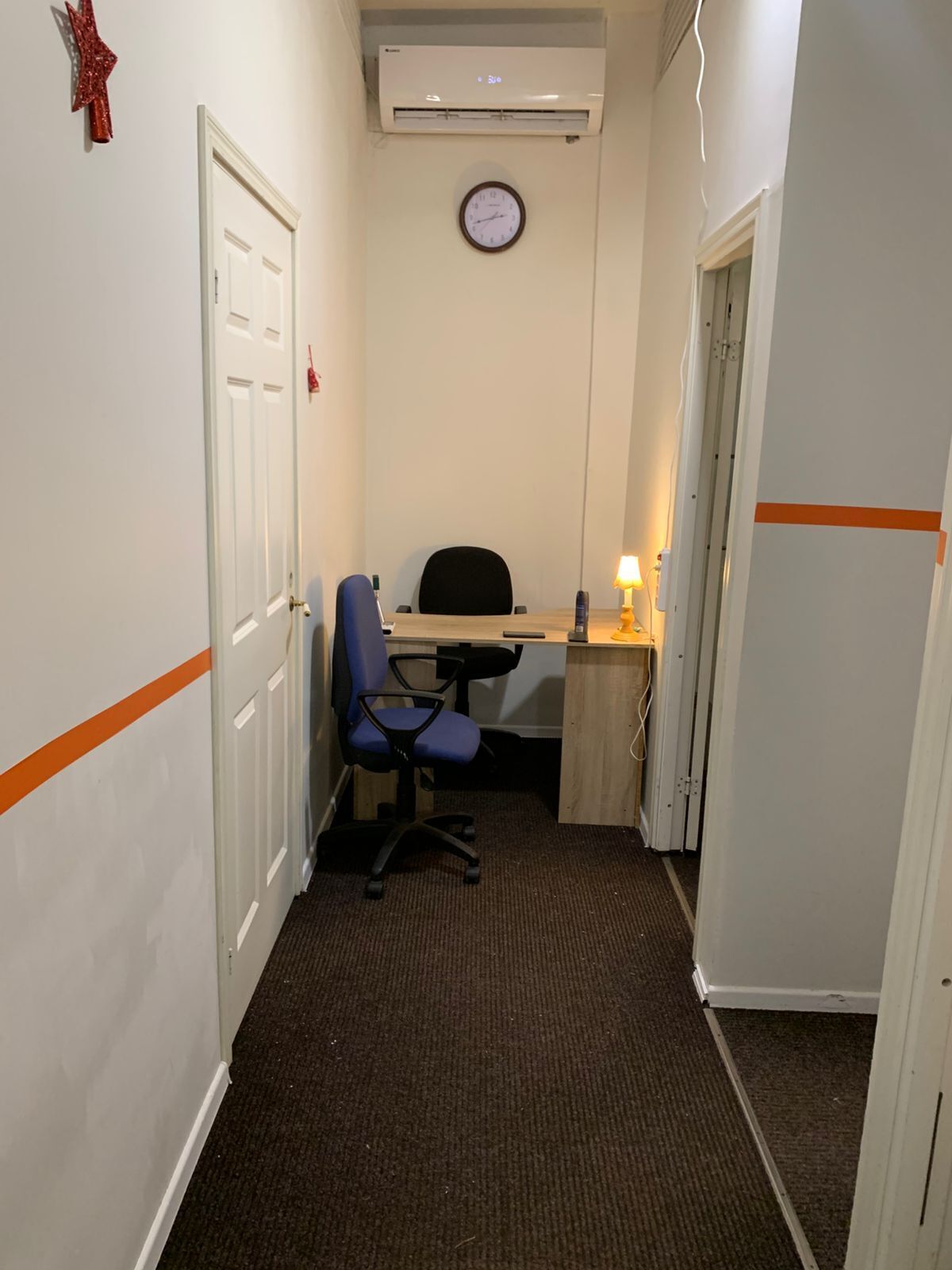 A narrow hallway with a desk, chair, and clock on the wall.