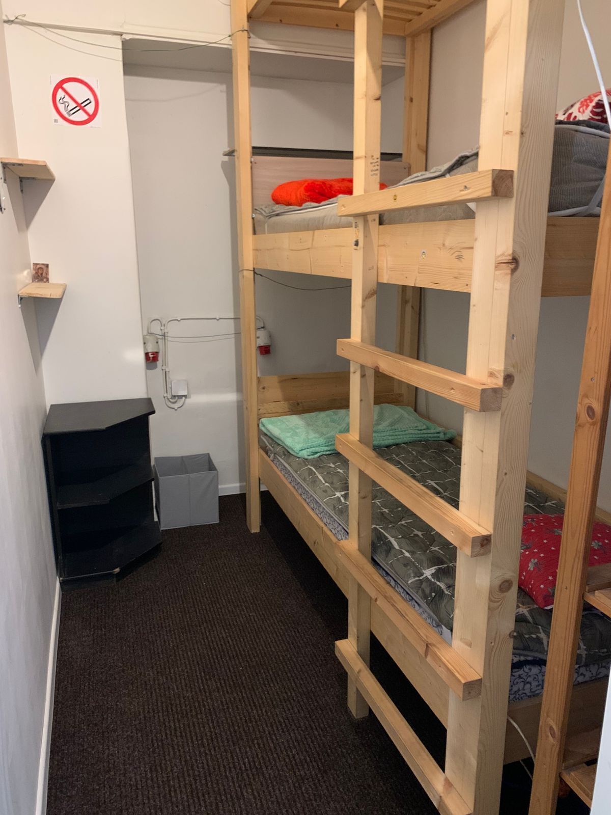 A bunk bed room with a wooden ladder, a small shelf, and a trash bin.