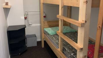 Habitación con literas, una escalera de madera, un estante pequeño y un cubo de basura.
