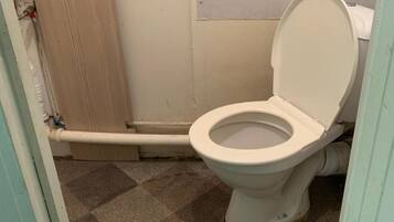 A bathroom with a toilet, a shower area, and a pair of black slippers on the floor.