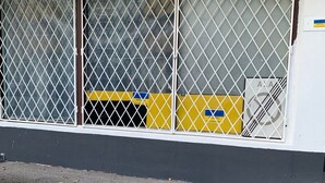 A building with a large window covered by metal bars. There is a yellow and blue sign on the window, and a white sign with the letters "A" and "A" on the right side. - Artishalico tallinn (Tallinn)
