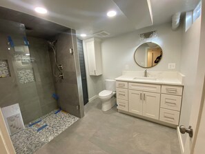 Un baño moderno con ducha de vidrio, inodoro y tocador con cajones y espejo.