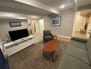Un salón moderno con un televisor de pantalla plana, un sofá gris, una mesa de centro marrón y un sillón gris.