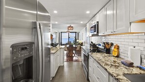 Cozinha moderna com frigorífico embutido, micro-ondas e máquina de café. Existe uma área de refeições com mesa e cadeiras.
