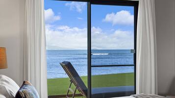 A hotel room with a large sliding glass door leading to a grassy area with a view of the ocean.