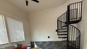 Un salon spacieux avec un grand canapé d’angle gris, une table basse et un escalier en colimaçon noir adossé au mur.