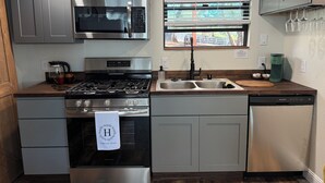 Une cuisine moderne dotée d’appareils électroménagers en acier inoxydable, de meubles de rangement gris et d’une fenêtre équipée de stores.
