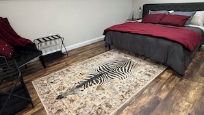 Une chambre avec un tapis à motifs zébrés, un lit avec une literie rouge et grise, une chaise et une petite table.