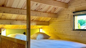 A wooden cabin room with a bed, a window, and a bunk bed. - Cosy escape in a small chalet 🏠 with outdoor jacuzzi! (Eslettes)