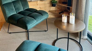 A modern living room with a green sofa, a small round table with candles, and a TV displaying a scenic landscape. - Cosy escape in a small chalet 🏠 with outdoor jacuzzi! (Eslettes)