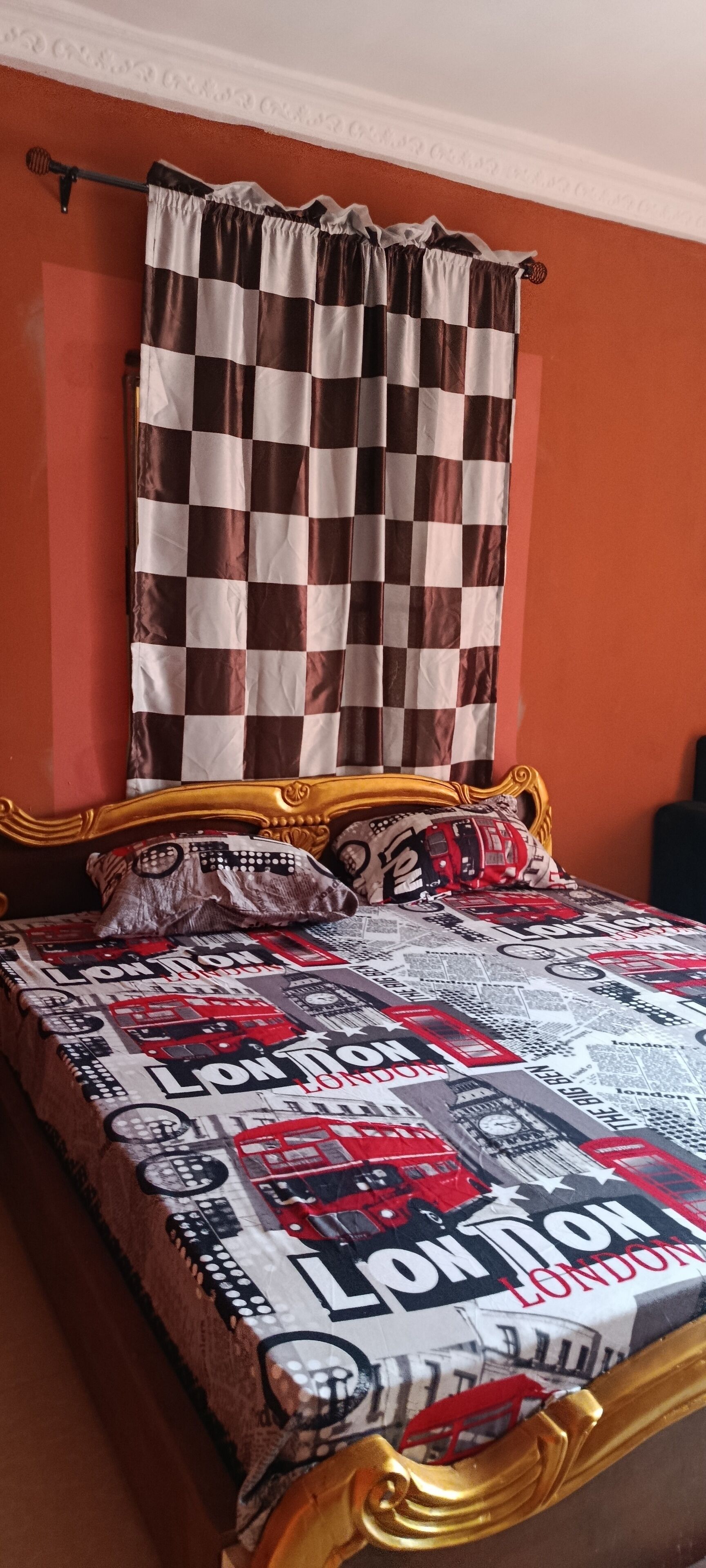 Ein Bett mit einem karierten Vorhang, einer gemusterten Tagesdecke und einem goldenen Kopfteil.