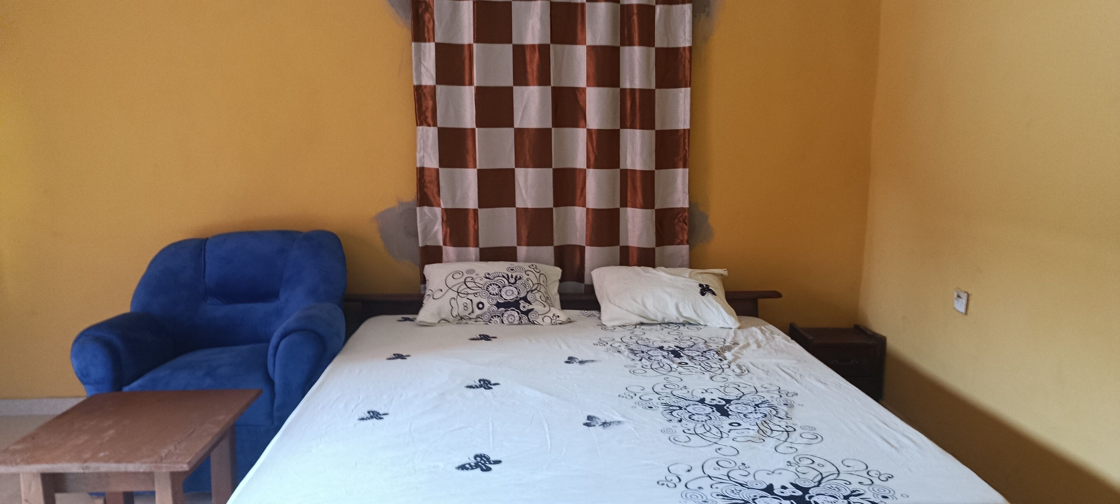 A bedroom with a bed, two pillows, a blue chair, and a wooden nightstand.