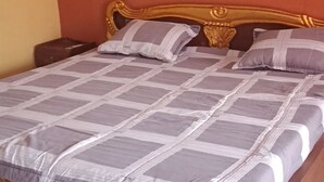 A bed with a patterned bedspread and two pillows, a wooden headboard, and a brown mattress. - Onimoba garden city  (Lagos)