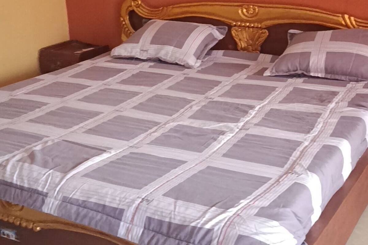 En seng med et mønstret sengetæppe, to puder, en træhovedgærde og en brun madras.