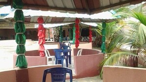Un área de estar al aire libre con mesas y sillas, rodeada de muros bajos y palmeras.