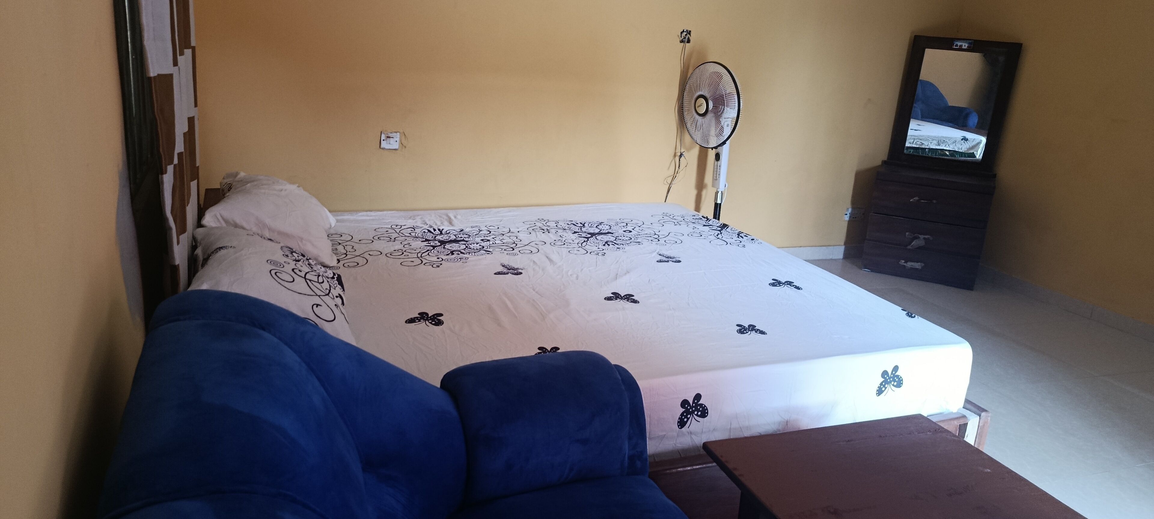 A bedroom with a bed, a fan, a dresser, and a TV on a dresser.