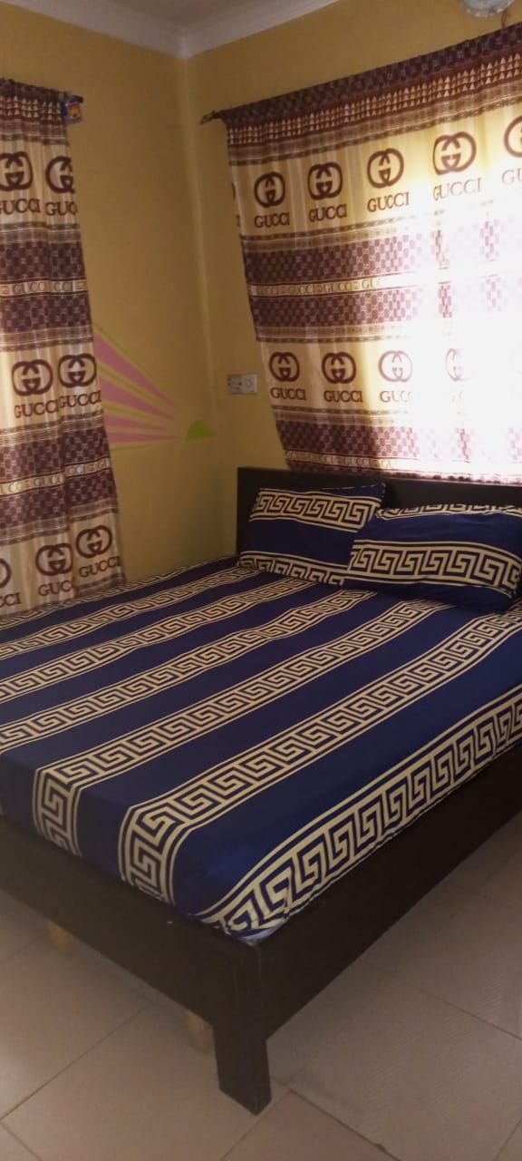A bed with a blue and white patterned bedspread and matching pillows, set in a room with yellow walls and curtains featuring a Gucci logo.