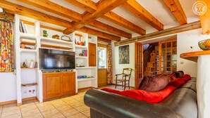 Ein gemütliches Wohnzimmer mit einem schwarzen Ledersofa, Holzbalken und einem Fernseher.