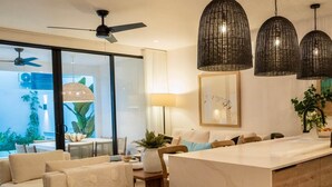 Una sala moderna con sofá, reposapiés y un comedor con mesa y sillas. Tres lámparas colgantes iluminan el comedor.
