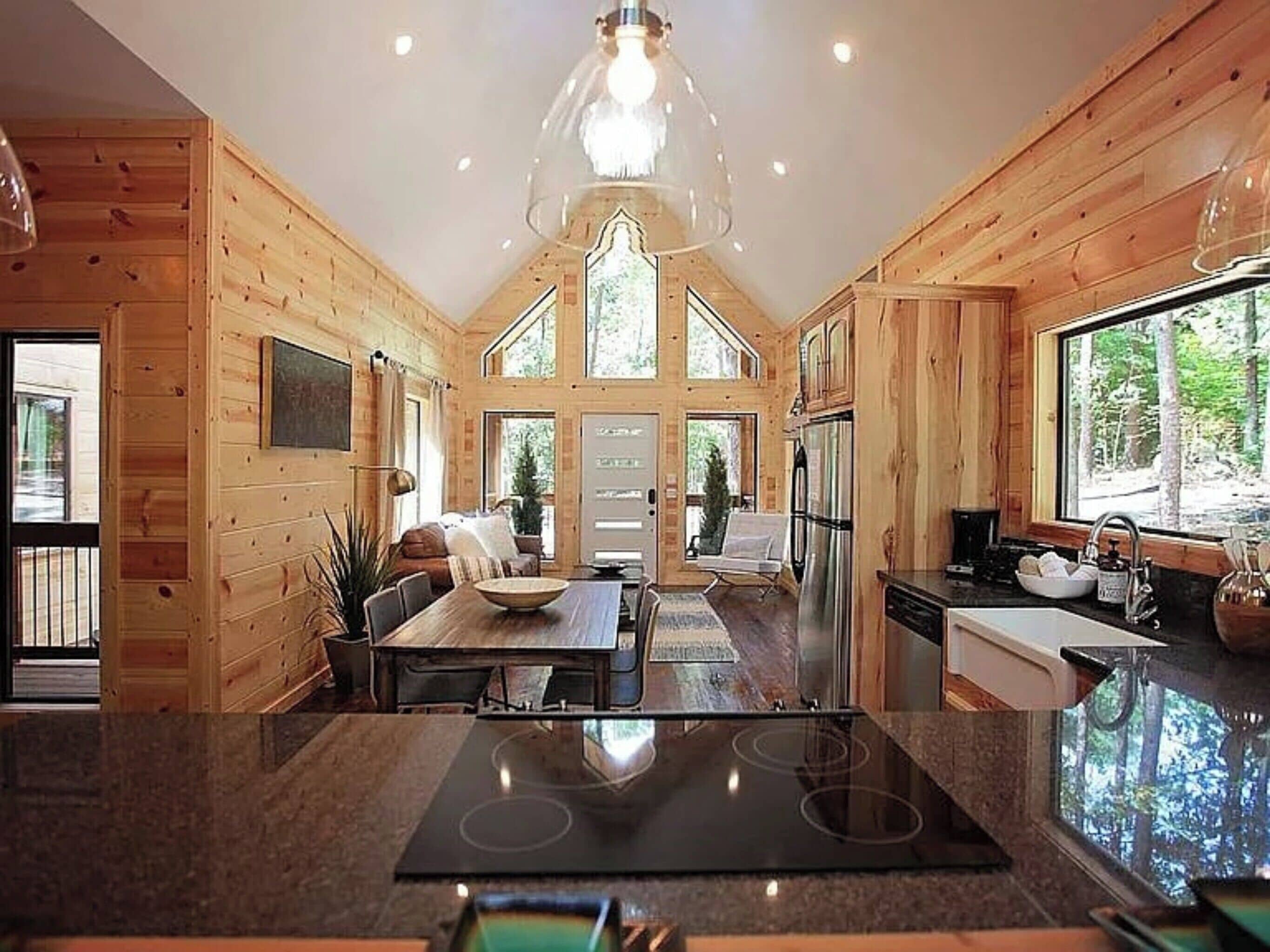 Ein modernes Blockhaus-Interieur mit Küche, Essbereich und großen Fenstern mit Blick auf den Wald.
