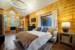 Une chambre spacieuse avec un grand lit, des murs en bois, un coin repas et une cuisine.