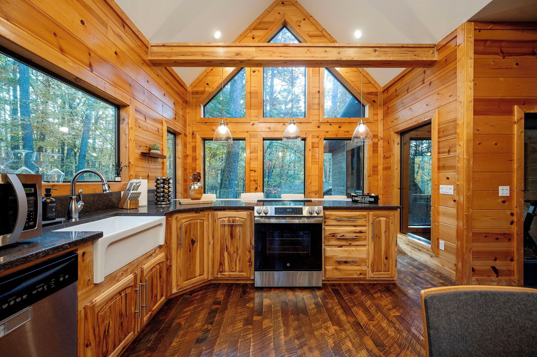 A log cabin kitchen with a large window, wooden cabinets, a stove, and a dishwasher.
