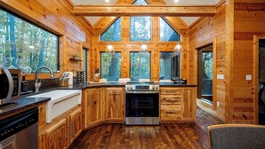 A log cabin kitchen with a large window, wooden cabinets, a stove, and a dishwasher. - Time to Relax - 2 king, 1 queen/2.5 bath, hot tub, fire pit, fireplaces (Broken Bow)
