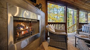 A cozy fireplace with a fire, wicker furniture, and a wooden deck with a railing. - Time to Relax - 2 king, 1 queen/2.5 bath, hot tub, fire pit, fireplaces (Broken Bow)