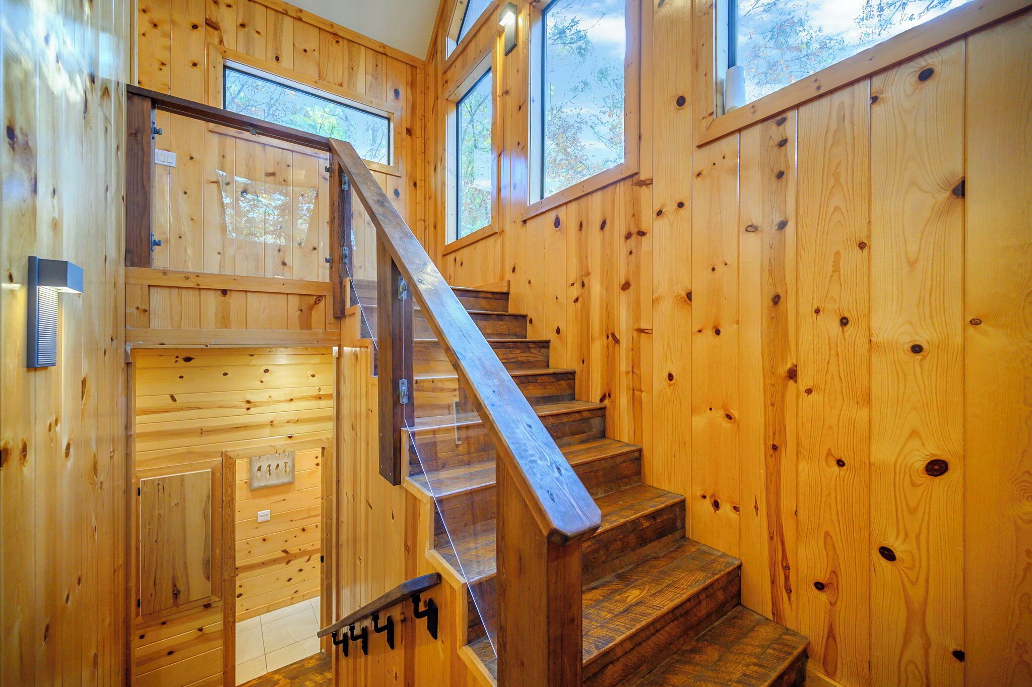 A wooden staircase with a glass railing leading to a landing.