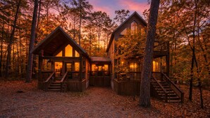 A cabin with a wooden exterior, multiple windows, and a staircase leading to the entrance. - Time to Relax - 2 king, 1 queen/2.5 bath, hot tub, fire pit, fireplaces (Broken Bow)