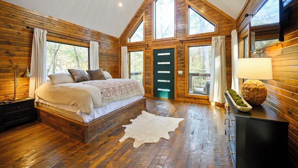 A bedroom with a wooden bed, a large window, and a view of the outdoors. - Time to Relax - 2 king, 1 queen/2.5 bath, hot tub, fire pit, fireplaces (Broken Bow)