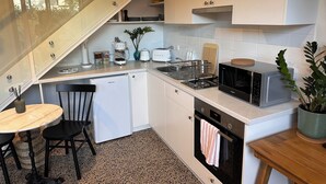 A compact kitchen with white cabinets, a small dining table, and a microwave. - Stylish Studio Apartment with Private Courtyard (Newtown)