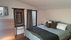 A bedroom with a bed, a nightstand, a wooden dresser, a window with curtains, and a wall-mounted rack. - Stylish Studio Apartment with Private Courtyard (Newtown)