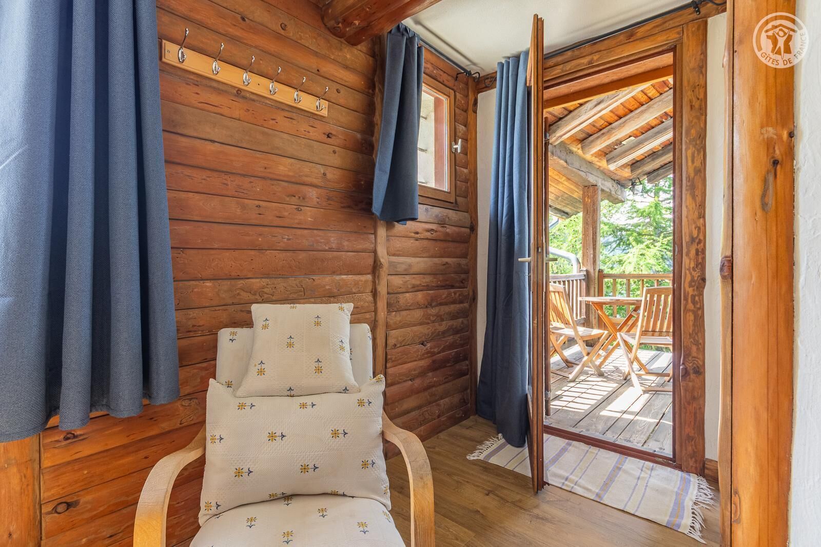 L’intérieur d’un chalet en bois, avec un lit, un porte-manteau et une vue sur une terrasse extérieure.