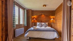 Quarto com painéis de madeira, uma cama, duas luminárias de cabeceira, um radiador e uma janela com cortinas.