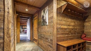 Interior rústico de madeira, com um banco e prateleiras, uma porta de madeira e um corredor que dá para outro quarto.