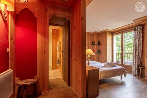 Une pièce en bois avec un lit, une table de chevet, une fenêtre donnant sur un paysage agréable et une porte menant à une autre pièce.