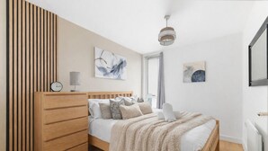 Una camera da letto con un letto in legno, un comodino, una sveglia a parete e due dipinti astratti.