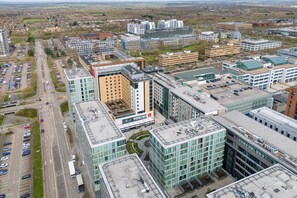 Luchtbeeld van een modern stedelijk gebied met verschillende gebouwen, waaronder een opvallend meerhoog gebouw met een centrale binnenplaats en een parkeerplaats met auto's.
