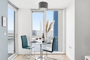 Een moderne eethoek met een glazen tafel, twee stoelen, een wijnfles en een vaas met veren van dodaarsgras.