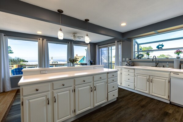 A modern kitchen with white cabinetry, a central island, and large windows offering a view of the ocean.