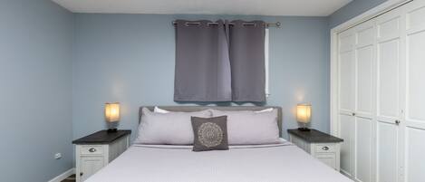 A bedroom with a bed, two bedside tables with lamps, a nightstand, a window with curtains, and a wardrobe.