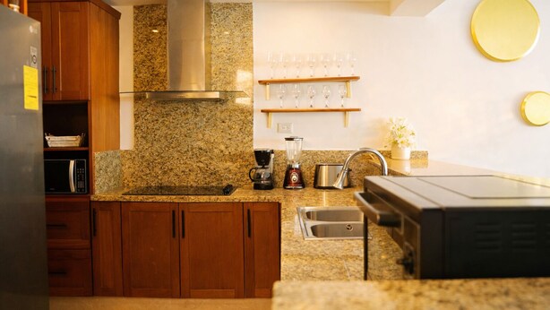 Una cocina con encimeras de granito, armarios de madera, una campana extractora de acero inoxidable, una cafetera y un lavabo.