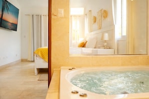 Une salle de bain avec une baignoire, un miroir, un lit et un tableau au mur.