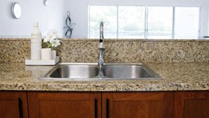 Una cocina con encimeras de granito, pileta de acero inoxidable, alacenas de madera y ventana con vistas.