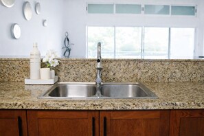 Una cocina con encimeras de granito, pileta de acero inoxidable, alacenas de madera y ventana con vistas.